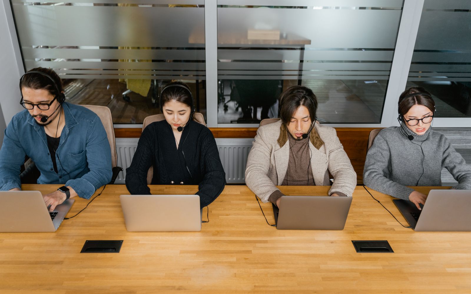 Four support staff in headsets working side by side at one long desk. Photo: MART PRODUCTION / Pexels.
