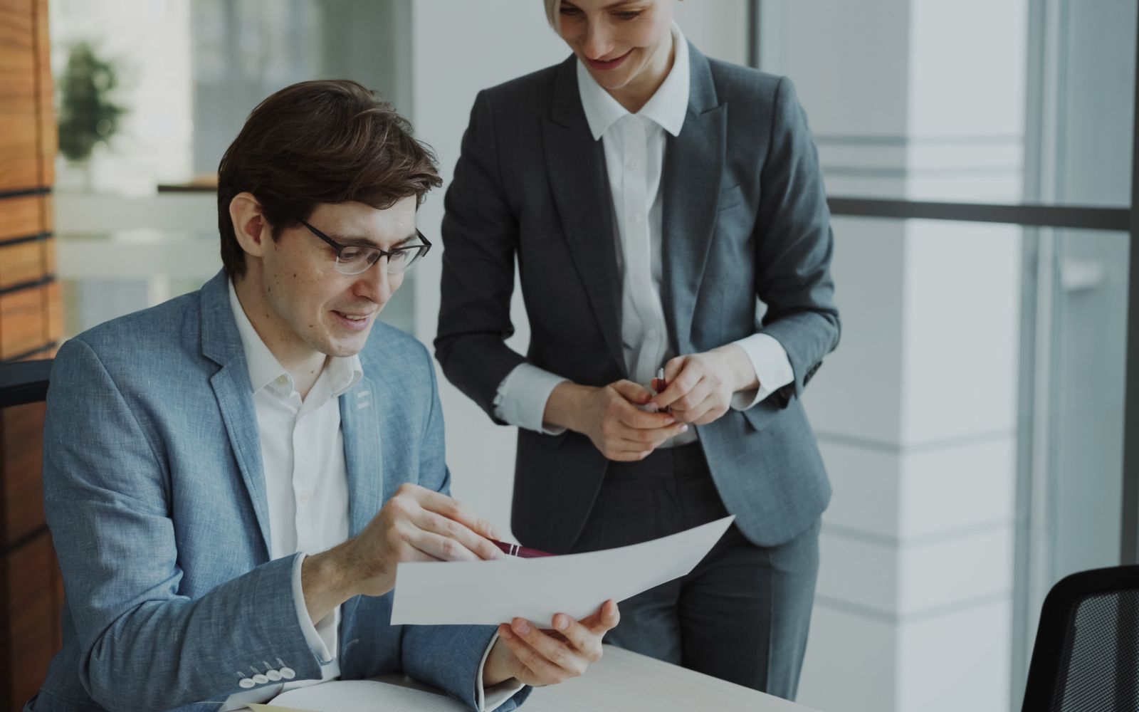 A seated colleague goes over a printed page while a colleague looks on. Photo: Vitaly Gariev / Pexels.