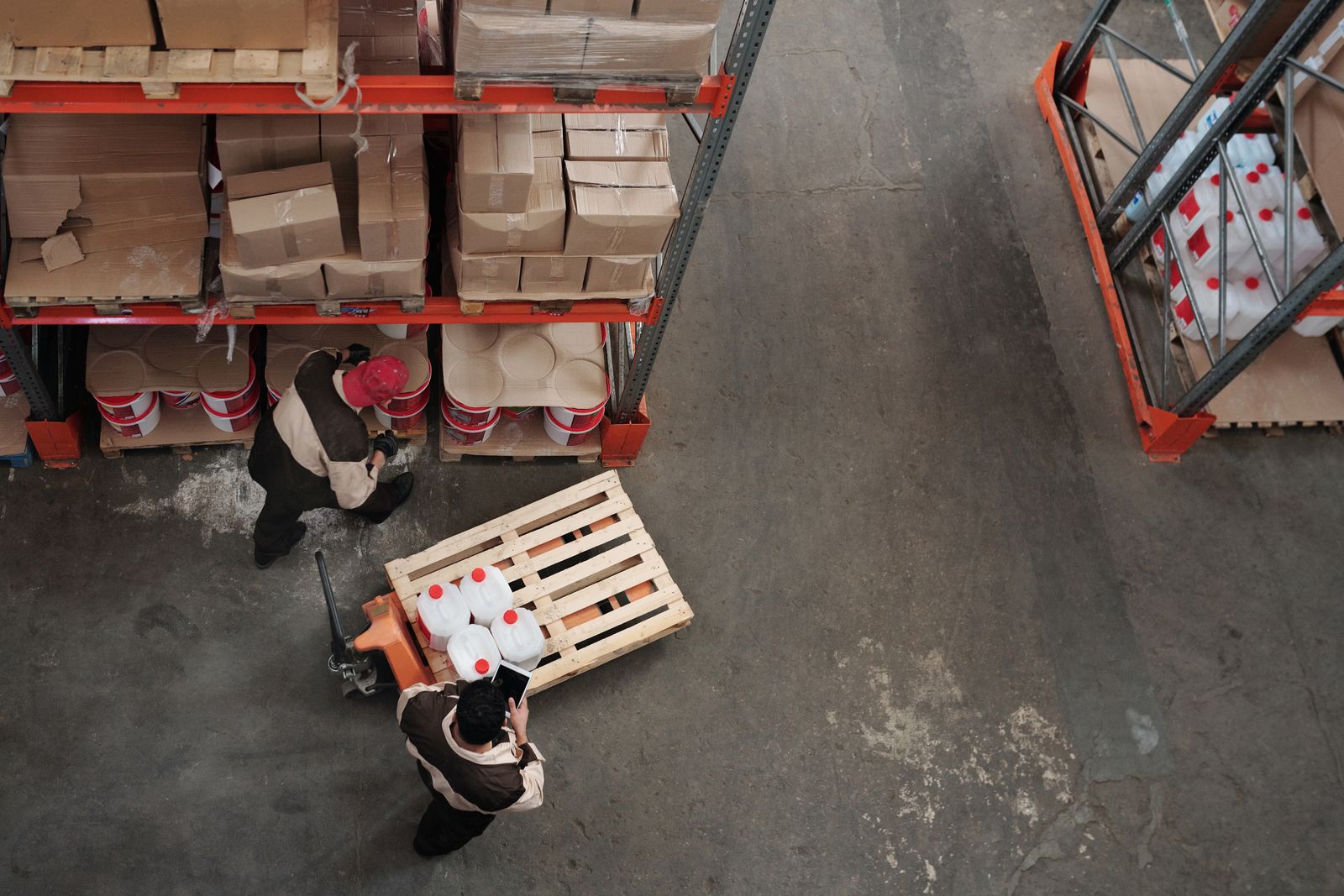 Two warehouse workers move a pallet in an aisle, seen from above. Photo: Tiger Lily / Pexels.