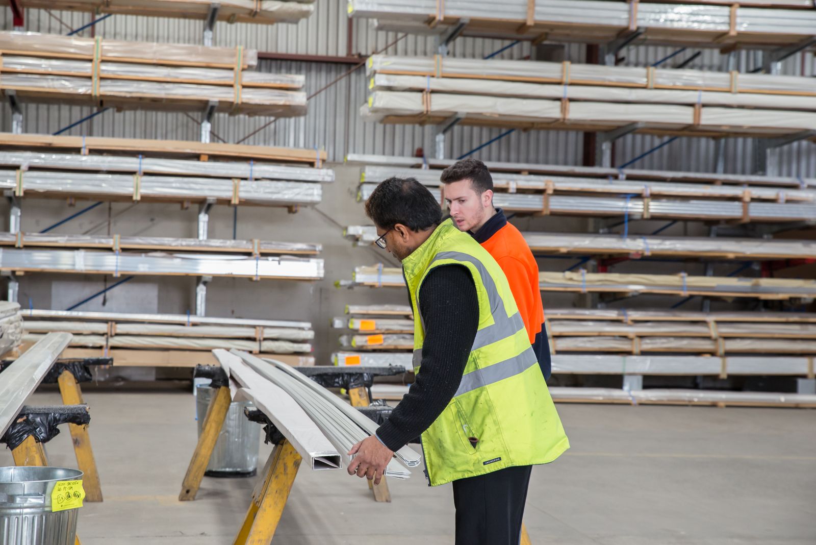 Two workers in a stockroom look over lengths of material at a trestle. Photo: James Richardson / Pexels.