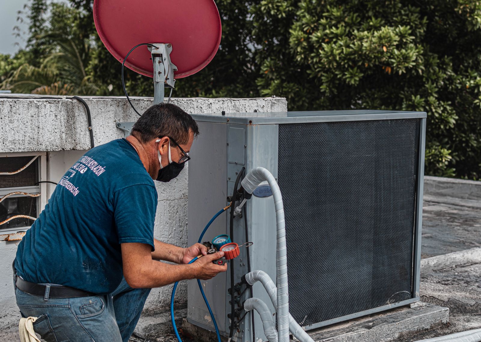 A refrigeration technician reads a manifold gauge connected to a rooftop condensing unit. Photo: José Andrés Pacheco Cortes / Pexels.