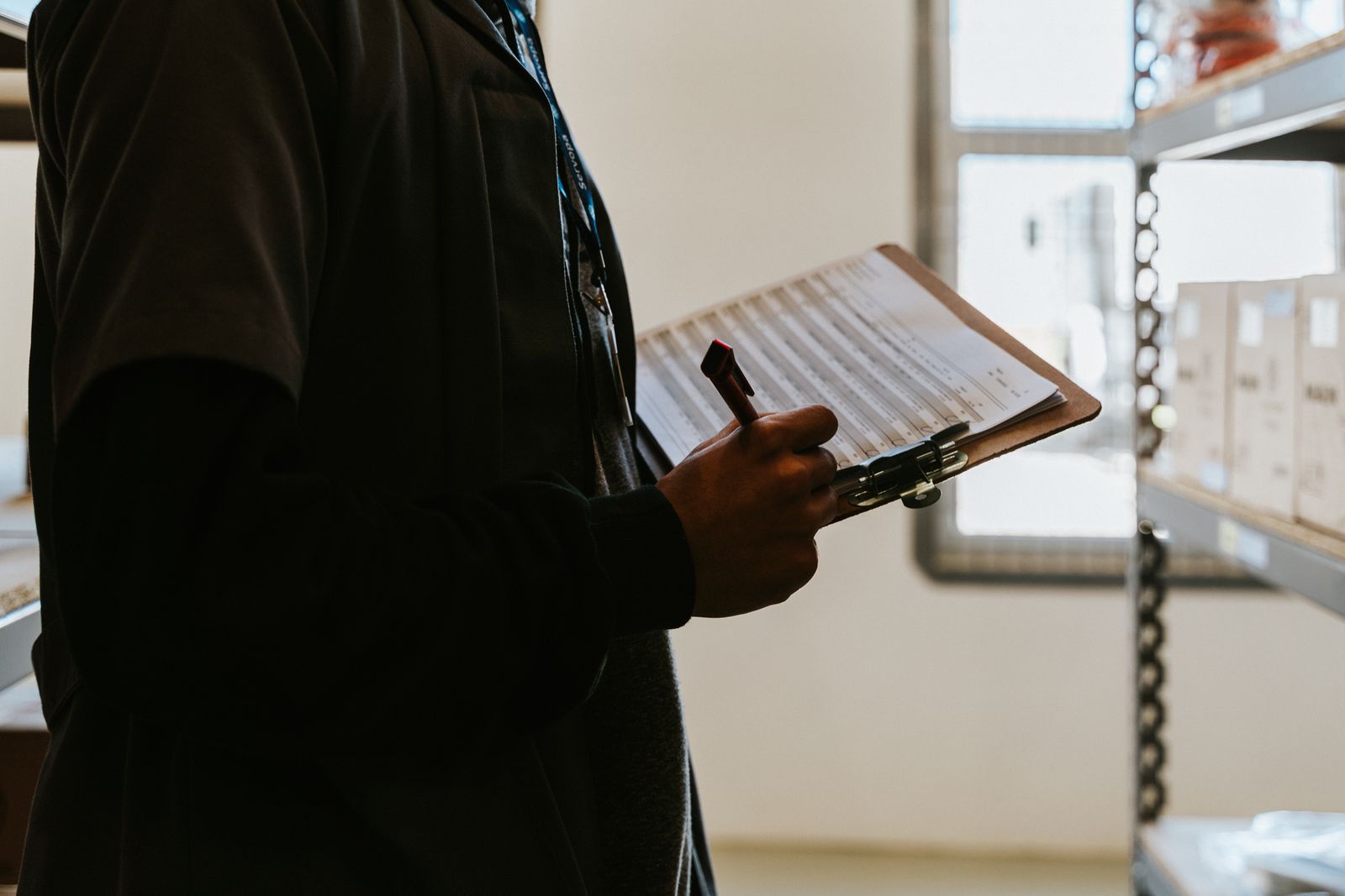 A shift lead in a stockroom reads a printed checklist on a clipboard. Photo: Daniel Andraski / Pexels.