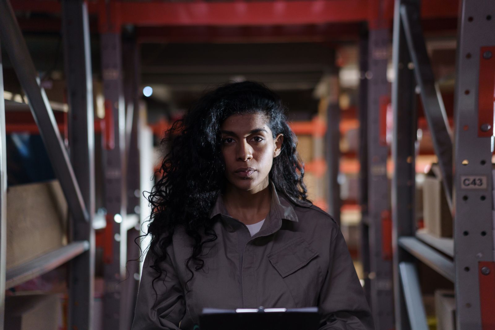 A warehouse worker stands in a shelving aisle holding a clipboard. Photo: cottonbro studio / Pexels.